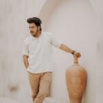 Fashionable man in smart casual wear poses with a clay vase in an elegant, minimalistic setting.