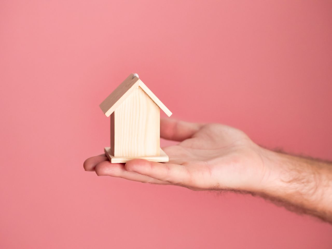 Crafting Captivating Headlines: Your awesome post title goes here Hand holding a small wooden house model against a soft pink background, symbolizing real estate and property investment.